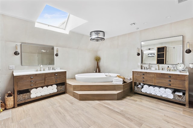 bathroom featuring visible vents, a garden tub, two vanities, a skylight, and a sink