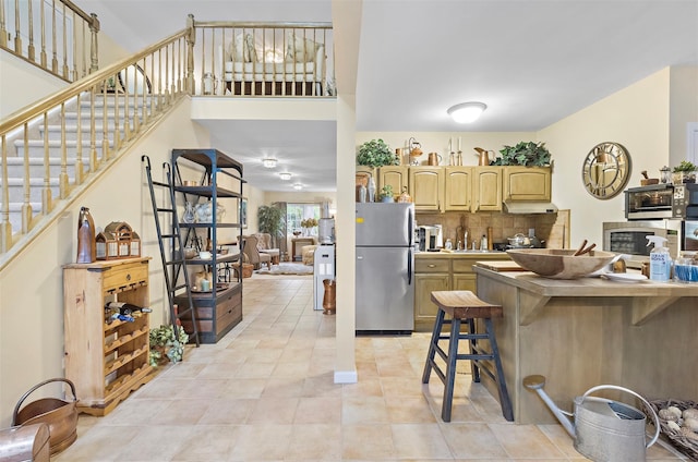 kitchen featuring backsplash, light brown cabinetry, a breakfast bar, light tile patterned floors, and freestanding refrigerator