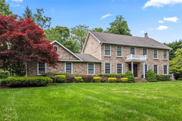 10 Fairway Dr, Port Jefferson, NY 11777 - colonial house featuring a balcony, a front yard, a chimney, roof with shingles, and brick siding