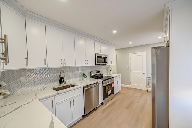 kitchen featuring backsplash, light wood-style flooring, stainless steel appliances, white cabinetry, and a sink