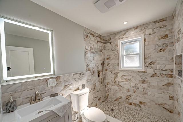 bathroom with vanity, tile walls, toilet, and a tile shower