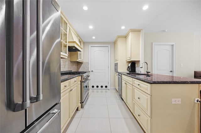 kitchen featuring light tile patterned floors, a peninsula, cream cabinets, stainless steel appliances, and a sink