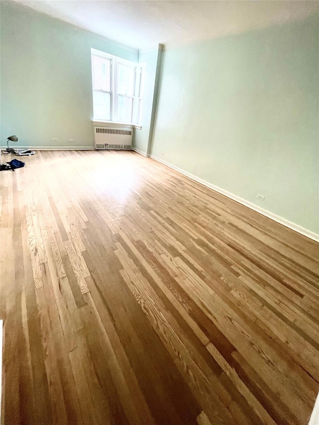 unfurnished room with baseboards, radiator, and wood finished floors