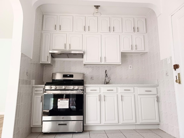 kitchen featuring light stone counters, stainless steel gas range, arched walkways, under cabinet range hood, and white cabinetry