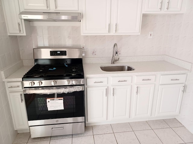 kitchen with under cabinet range hood, stainless steel range with gas stovetop, white cabinets, and a sink