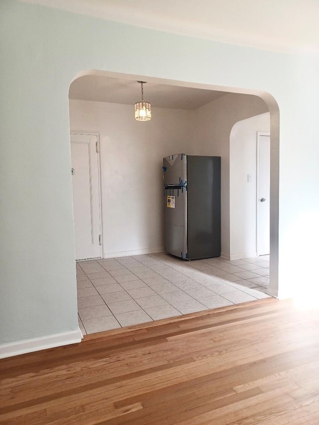 empty room featuring arched walkways, light wood finished floors, and baseboards