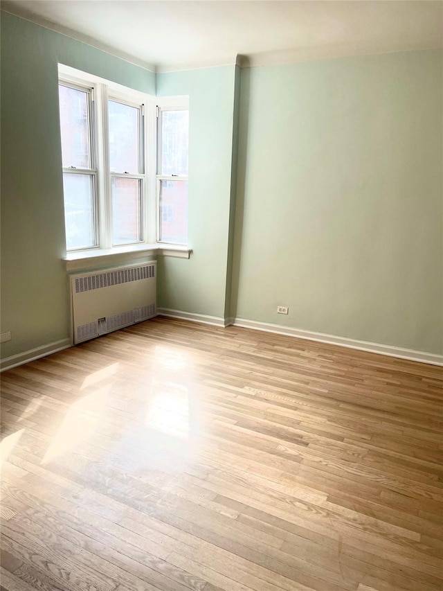 unfurnished room featuring radiator, baseboards, and light wood finished floors