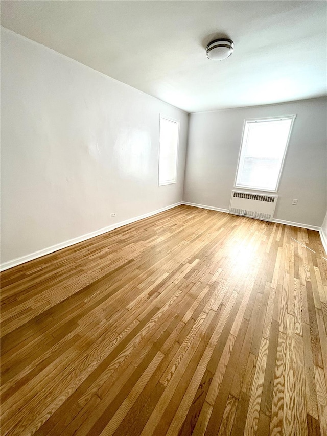 spare room featuring a wealth of natural light, radiator, baseboards, and hardwood / wood-style flooring