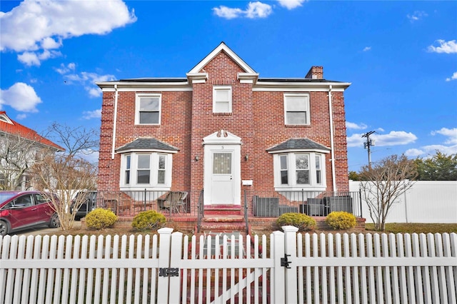 view of front of property with a fenced front yard, brick siding, a chimney, and a gate