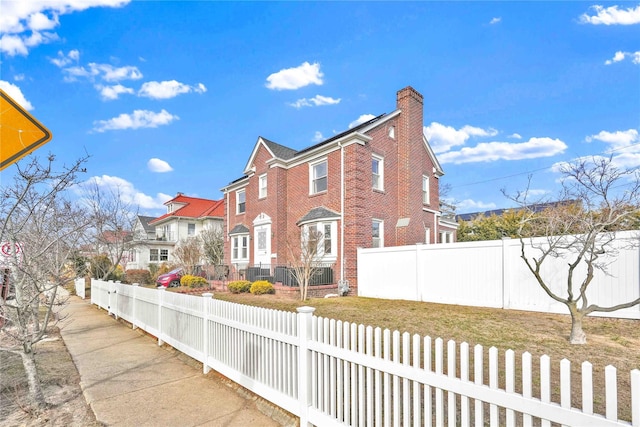 view of property exterior featuring a residential view, brick siding, fence private yard, and a chimney