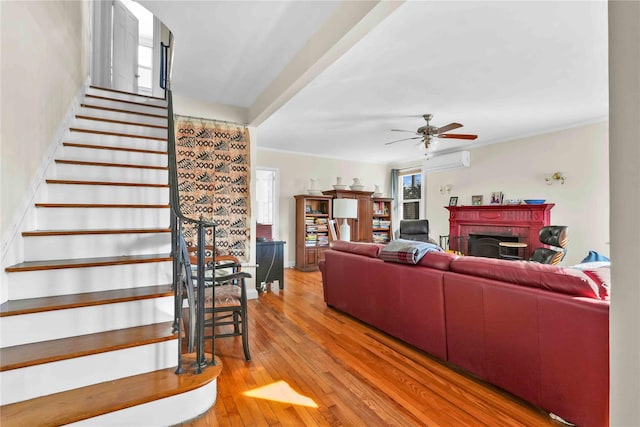 living room featuring stairway, a ceiling fan, a fireplace, a wall mounted air conditioner, and light wood-type flooring