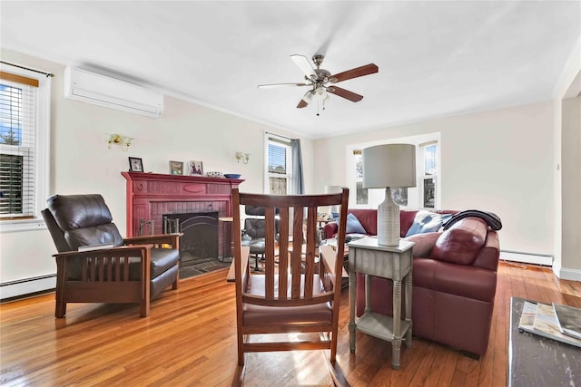 living area with a wall mounted air conditioner, light wood-style flooring, baseboard heating, a brick fireplace, and ceiling fan