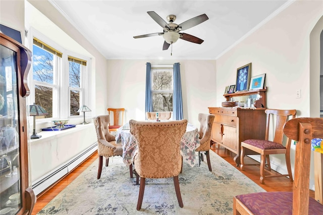 interior space featuring ornamental molding, baseboard heating, wood finished floors, arched walkways, and a ceiling fan