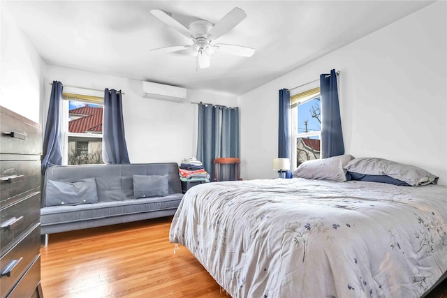 bedroom with multiple windows, a ceiling fan, a wall unit AC, and wood finished floors