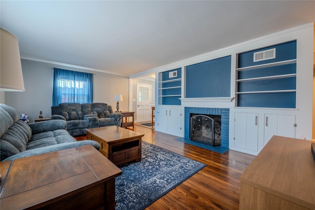 living area with a brick fireplace, wood finished floors, visible vents, and ornamental molding