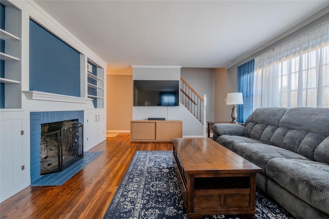 living room featuring built in features, stairs, ornamental molding, a fireplace, and wood finished floors