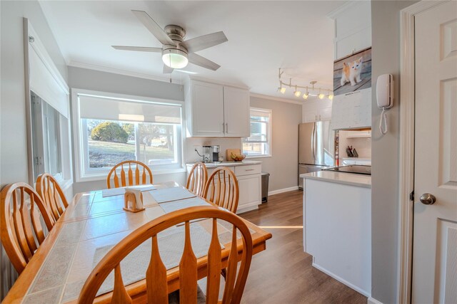 dining space with a ceiling fan, baseboards, light wood finished floors, ornamental molding, and track lighting