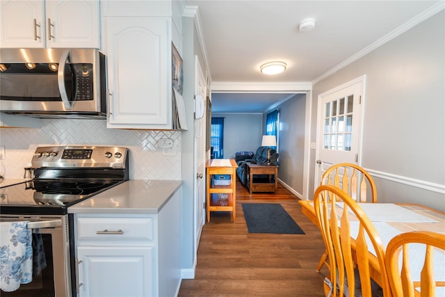 kitchen with wood finished floors, ornamental molding, white cabinets, appliances with stainless steel finishes, and backsplash