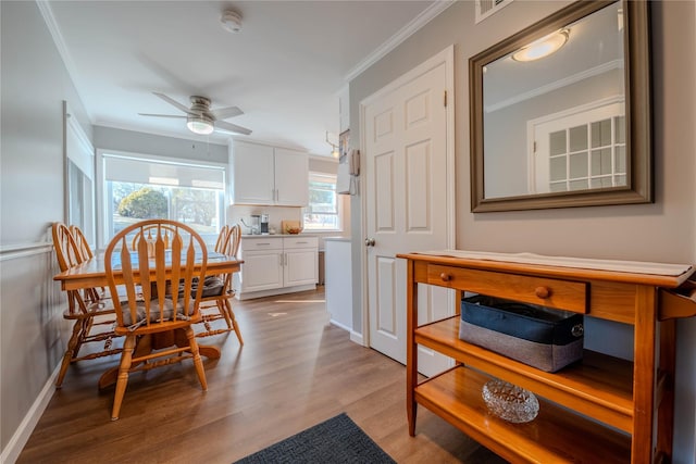 dining room featuring light wood-type flooring, visible vents, ornamental molding, a ceiling fan, and baseboards