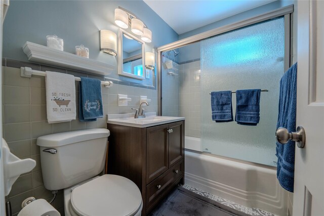 full bathroom featuring combined bath / shower with glass door, toilet, tile walls, and vanity