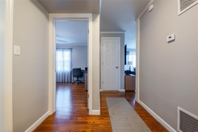 hallway featuring dark wood finished floors, baseboards, visible vents, and ornamental molding