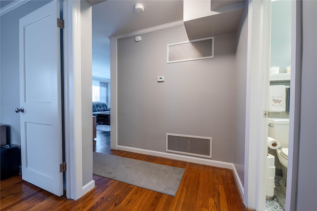 corridor with visible vents, baseboards, wood finished floors, and ornamental molding