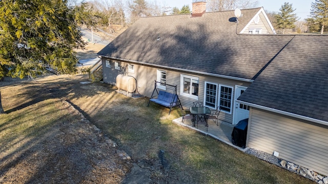 rear view of property with a patio, a lawn, a chimney, and a shingled roof