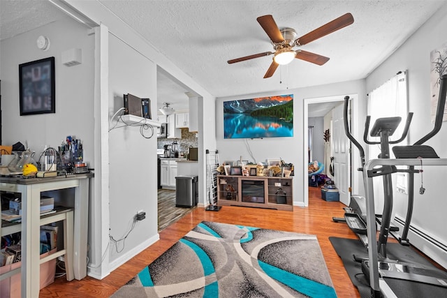 workout room featuring light wood-style flooring, a textured ceiling, and ceiling fan