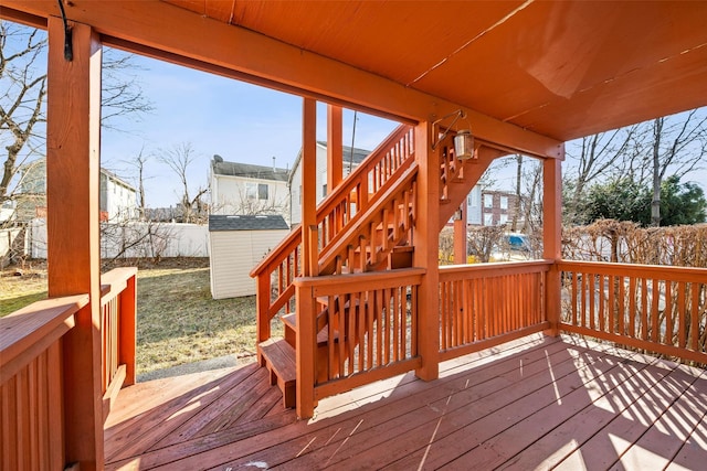 wooden deck with a storage unit, an outbuilding, stairs, and fence