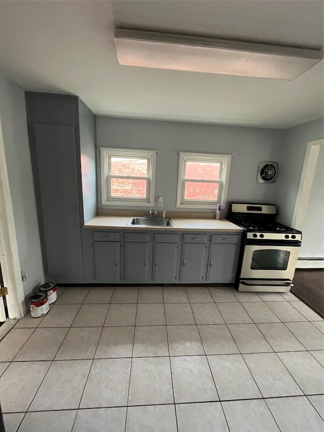 kitchen with gray cabinetry, a baseboard heating unit, stainless steel range with gas stovetop, light tile patterned floors, and a sink