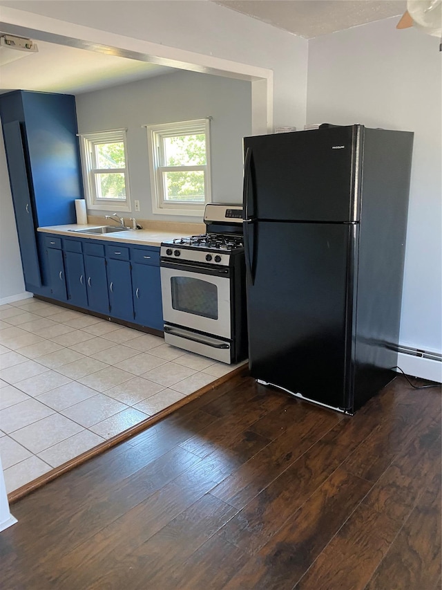 kitchen featuring light wood finished floors, stainless steel range with gas cooktop, freestanding refrigerator, blue cabinets, and a sink