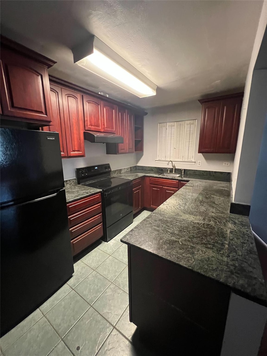 kitchen with a peninsula, a sink, black appliances, dark brown cabinets, and under cabinet range hood