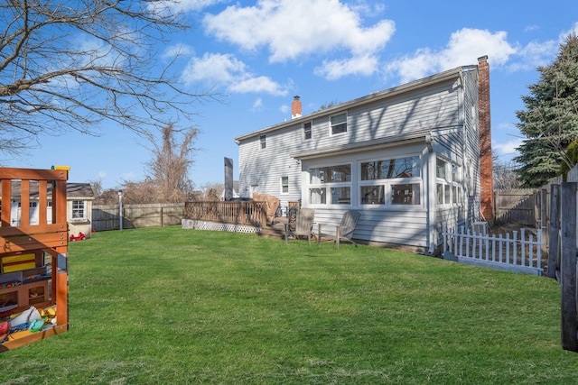 back of house featuring a wooden deck, a lawn, a chimney, and a fenced backyard