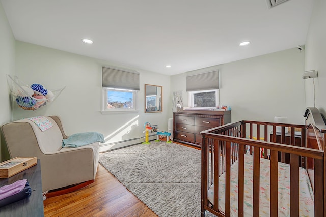 bedroom featuring recessed lighting, a baseboard heating unit, a nursery area, and wood finished floors