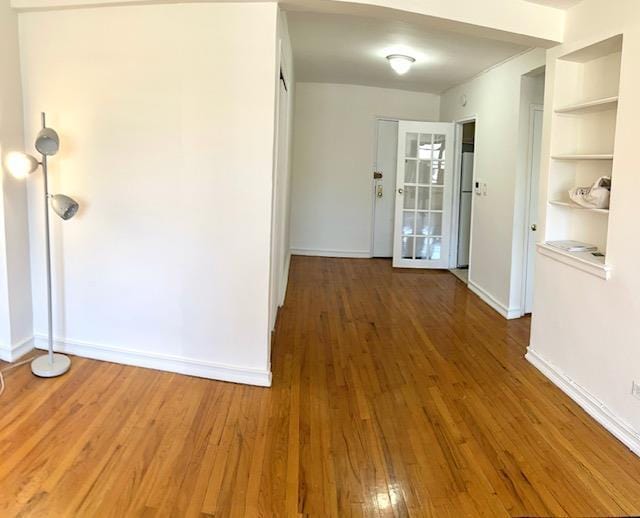 hall featuring built in features, baseboards, and wood finished floors