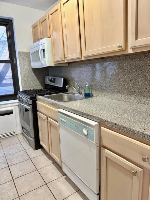 kitchen with white appliances, light tile patterned floors, light brown cabinetry, a sink, and backsplash