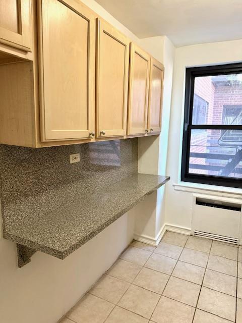 kitchen featuring light tile patterned floors, baseboards, radiator heating unit, light brown cabinetry, and tasteful backsplash