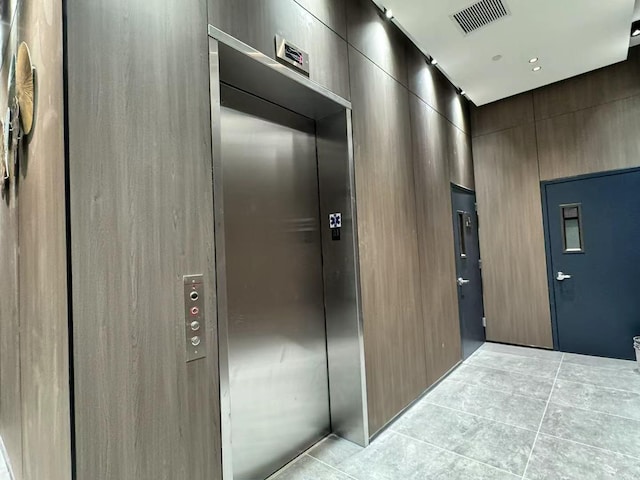 hall with light tile patterned flooring, visible vents, and elevator