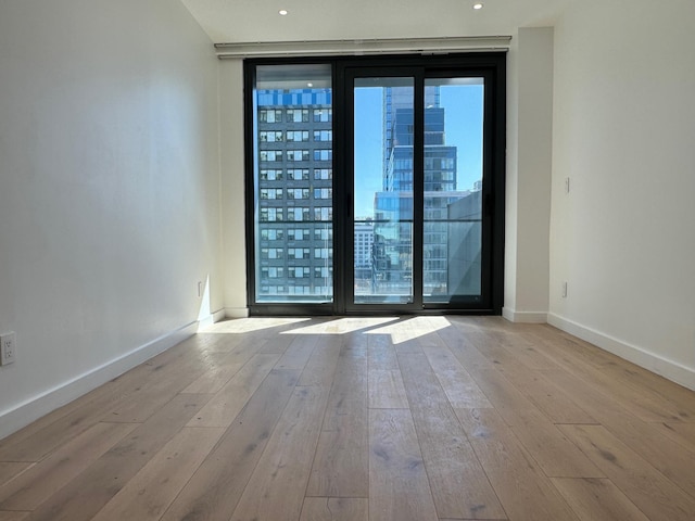 empty room featuring baseboards, floor to ceiling windows, recessed lighting, a view of city, and wood-type flooring