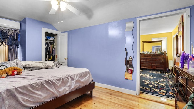 bedroom with light wood finished floors, ceiling fan, baseboards, vaulted ceiling, and a wall mounted AC