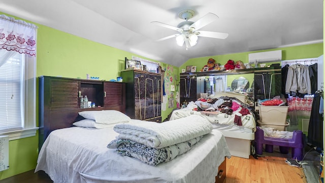 bedroom featuring ceiling fan, a wall unit AC, wood finished floors, and vaulted ceiling