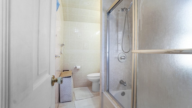 bathroom with tile patterned flooring, tile walls, toilet, and combined bath / shower with glass door