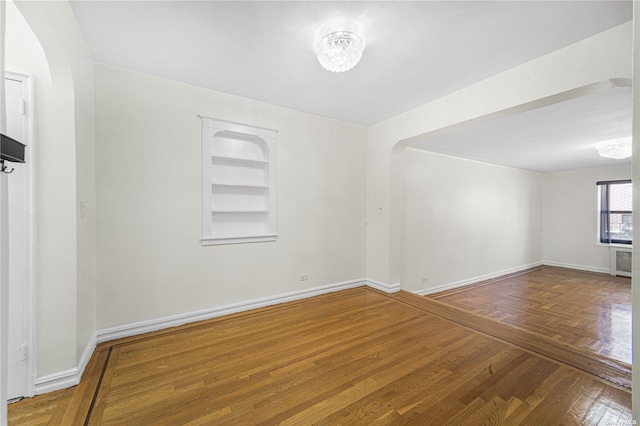 unfurnished room with arched walkways, built in features, baseboards, and wood finished floors