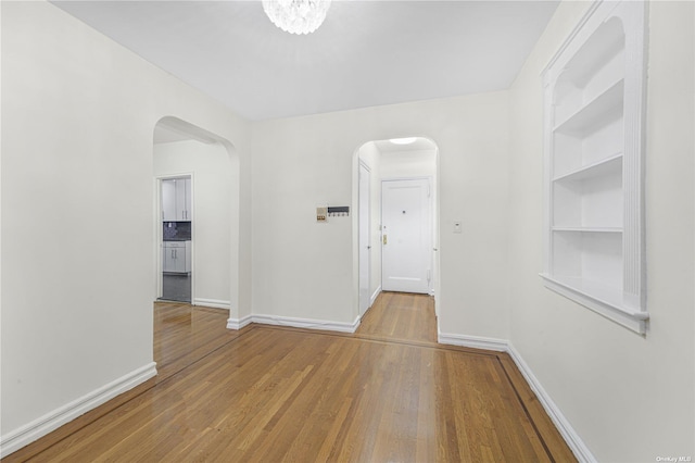 interior space featuring arched walkways, built in shelves, baseboards, and wood finished floors