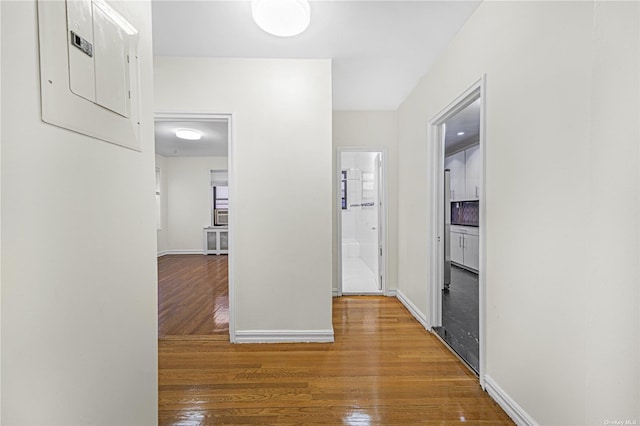 hallway featuring electric panel, wood finished floors, and baseboards