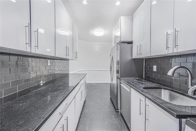 kitchen featuring a sink, dark stone counters, decorative backsplash, white cabinetry, and stainless steel dishwasher