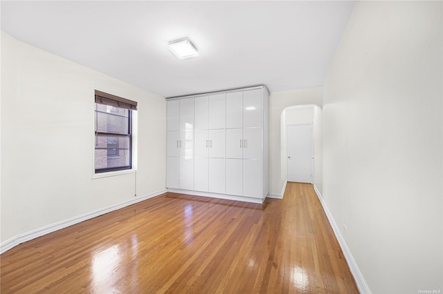 unfurnished bedroom featuring baseboards, arched walkways, and hardwood / wood-style flooring