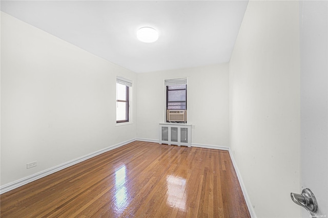 empty room with cooling unit, radiator heating unit, baseboards, and wood-type flooring