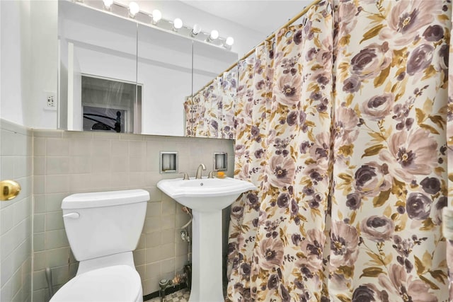 full bathroom featuring a sink, wainscoting, curtained shower, tile walls, and toilet