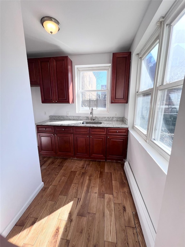 kitchen with a sink, dark wood finished floors, baseboards, baseboard heating, and dark brown cabinets